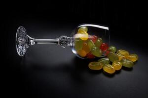 A lot of candy canes are scattered from an overturned glass goblet. Multi-colored candies in a glass on a black background. Marmalade candies. photo