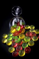 A lot of candy canes are scattered from an overturned glass goblet. Multi-colored candies in a glass on a black background. photo