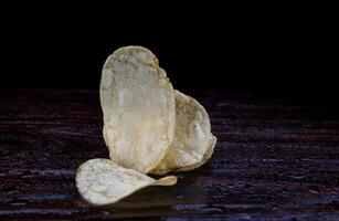 Potato chips on a dark background. Chips on a wooden board photo