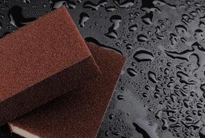 Melamine sponge on a black wet background. Beautiful drops of water around a melamine sponge. photo