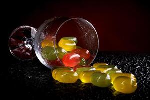 A lot of candy canes are scattered from an overturned glass goblet. Multi-colored candies in a glass on a black background. Marmalade candies. photo