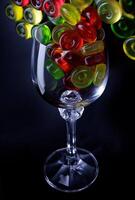 Many lollipops spill out from an overturned glass goblet. Multi-colored candies in a glass on a black background. photo