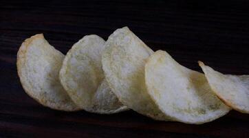 Potato chips on a dark background. Chips on a wooden board photo