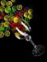 A lot of lollipops are scattered from an overturned glass goblet. Multi-colored candies in a glass. photo