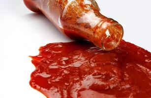 tomate salsa . un vaso botella con salsa de tomate y un charco de salsa de tomate derramado alrededor él. foto