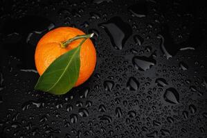 Ripe juicy tangerine on a black background with water drops. photo