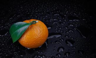 Ripe juicy tangerine on a black background with water drops. photo