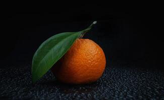 Ripe juicy tangerine on a black background with water drops. photo