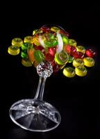 A lot of candy canes are scattered from an overturned glass goblet. Multi-colored candies in a glass on a black background. photo