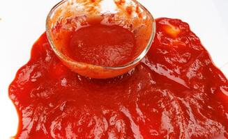 Tomatnyy sous . Steklyannaya chashka s ostatkami ketchupa i razlityy vokrug ketchup . photo