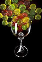 Many lollipops spill out from an overturned glass goblet. Multi-colored candies in a glass on a black background. photo