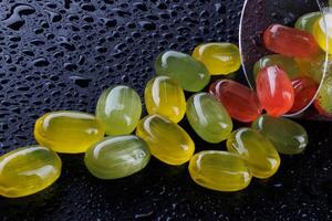 A lot of candy canes are scattered from an overturned glass goblet. Multi-colored candies in a glass on a black background. Marmalade candies. photo