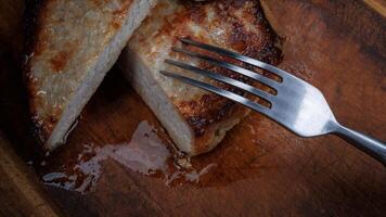 Roasted pork entrecote cut into pieces on a wooden cutting board. Fork in meat. photo