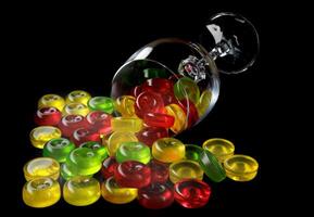 Many lollipops spill out from an overturned glass goblet. Multi-colored candies in a glass on a black background. photo