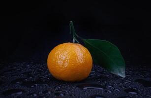 Ripe juicy tangerine on a black background with water drops. photo