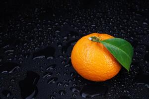 Ripe juicy tangerine on a black background with water drops. photo