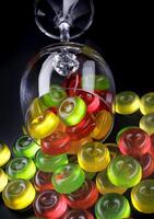 A lot of candy canes are scattered from an overturned glass goblet. Multi-colored candies in a glass on a black background. photo