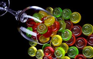 A lot of candy canes are scattered from an overturned glass goblet. Multi-colored candies in a glass on a black background. photo