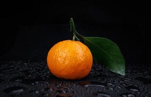 Ripe juicy tangerine on a black background with water drops. photo