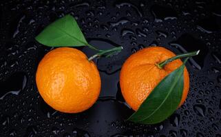 Two ripe juicy tangerines on a black background with drops of water. photo