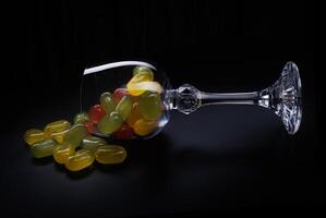 A lot of candy canes are scattered from an overturned glass goblet. Multi-colored candies in a glass on a black background. Marmalade candies. photo