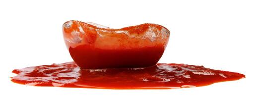 Tomato sauce . Glass cup with ketchup and a puddle of ketchup spilled around it isolated on a white background. photo