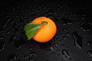 Ripe juicy tangerine on a black background with water drops. photo