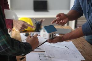 ingenieros son consultante el equipo a diseño un arquitectónico estructura para clientela con planos y edificio modelos a trabajo a oficina. foto