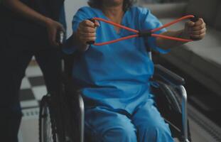 Personal trainer assisting senior woman with resistance band. Rehabilitation physiotherapy worker helping old patient at nursing home. Old woman with stretch band being coached by physiotherapist. photo