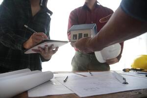 ingenieros son consultante el equipo a diseño un arquitectónico estructura para clientela con planos y edificio modelos a trabajo a oficina. foto