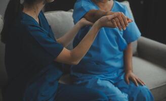 Old woman training with physiotherapist using dumbbells at home. Therapist assisting senior woman with exercises in nursing home. Elderly patient using dumbbells with outstretched arms. photo