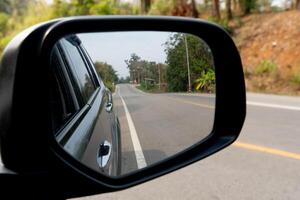 Reflection of the road in the side mirror of a car. Rear view mirror of car on asphalt road background. Copy space and blurred of roads in provincial areas photo