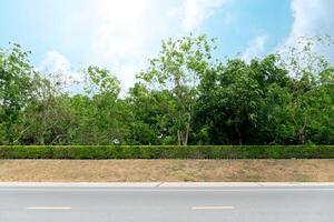 Landscape view of asphalt road and with mound of dirt blocks the road line and is covered with modified grass. Background of trees under blue sky and white clouds. photo