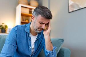 Closeup of man suffering from headache at home, touching his temples, copy space, blurred background. Migraine, headache, stress, tension problem, hangover concept photo