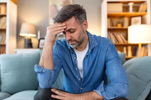 Closeup of man suffering from headache at home, touching his temples, copy space, blurred background. Migraine, headache, stress, tension problem, hangover concept photo