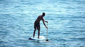 hombre cenar mar. fuerte atlético hombre aprende a paleta cenar en pie en tablero en abierto mar Oceano en soleado día. verano fiesta vacaciones y viaje concepto. aéreo vista. lento movimiento video