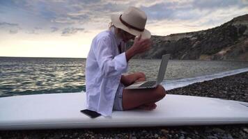 Digital nomad, Business woman working on laptop by the sea. Pretty lady typing on computer by the sea at sunset, makes a business transaction online from a distance. Freelance, remote work on vacation video