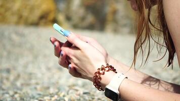 vrouw met smartphone. detailopname van vrouw handen Holding verticaal mobiel telefoon en vegen omhoog vinger toepassing bladzijde tegen achtergrond van zee en strand video