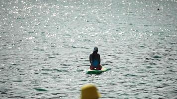 zee vrouw sup. silhouet van gelukkig positief jong vrouw in blauw bikini, surfing Aan groen sup bord door kalmte water oppervlak. idyllisch zonsondergang. actief levensstijl Bij zee of rivier. langzaam beweging video