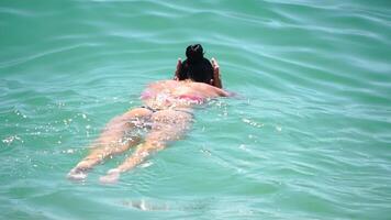 Woman swimming in calm sea at sunset, slow-motion, back view. Concept of body image and fitness, enjoying a serene beach. Happy woman with perfect fit body enjoys sea beach video