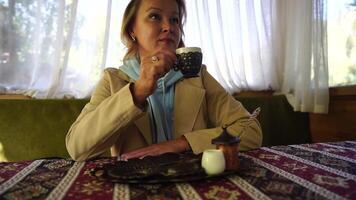 Woman pouring Turkish coffee from cezve into cup. Closeup slow motion shot of female hand with cup on square plate, on table in cafe outdoor. Traditional hot unfiltered coffee served in restaurant video