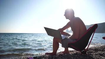 Mann Laptop Meer. Arbeiten entfernt auf Strand. Mann wirft Weg Laptop, männlich Freiberufler erleichtert Stress von Arbeit zu wiederherstellen Leben Gleichgewicht. freiberuflich, Fernbedienung Arbeit auf Urlaub. schleppend Bewegung video