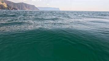 Meer Wasser Oberfläche. Kamera fliegt Über das Ruhe azurblau Meer mit vulkanisch felsig Ufer auf Hintergrund. niemand. Urlaub Erholung Konzept. abstrakt nautisch Sommer- Ozean Natur. schleppend Bewegung. schließen oben video