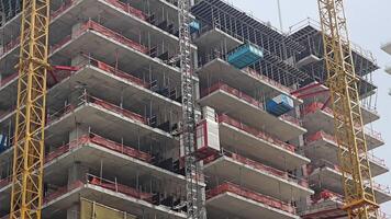 urbano costruzione luogo con Torre gru, avvicinamento Visualizza di un' a più piani edificio sotto costruzione con un' Torre gru e sicurezza barriere. video