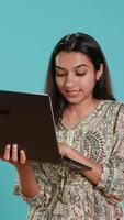 vertikal kvinna komponera e-post, försiktigt skriver på bärbar dator tangentbord, kämpar till tror av Vad till skriva. indisk person sändning post uppkopplad, brainstorming meddelande aning, studio bakgrund, kamera en video