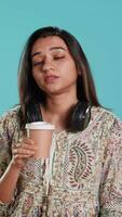 vertical soñoliento mujer bostezando, bebiendo café a ganancia energía y obtener eliminar de dolor de cabeza. agotado persona sensación fatigado después insomne noche, Bebiendo cafeinado bebida, estudio fondo, cámara un video