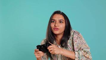 Gamer annoyed after losing online multiplayer videogame, being defeated by rival players. Indian woman upset after seeing game over message, holding controller, studio background, camera B video