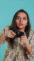 verticaal gelukkig gamer vieren na winnend spel Aan gaming troosten, studio achtergrond. verheugd vrouw opscheppen na wezen zegevierend in videogame, verslaan allemaal vijanden gebruik makend van gamepad, camera een video