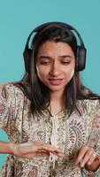 Vertical Indian woman playing music, having fun moving on rhythm, pretending to use turntables. Upbeat DJ wearing headphones, producing beats, isolated over studio background, camera A video