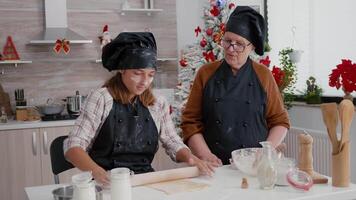 grand-mère enseignement petite fille Comment préparer délicieux Noël pain d'épice dessert fabrication biscuits pâte en utilisant roulant broche. content famille profiter cuisine célébrer Noël vacances video